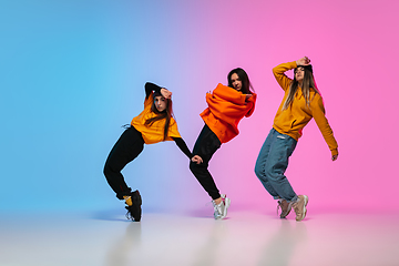 Image showing Girls dancing hip-hop in stylish clothes on gradient background at dance hall in neon light.