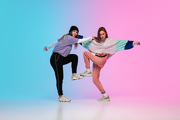 Image showing Girls dancing hip-hop in stylish clothes on gradient background at dance hall in neon light.