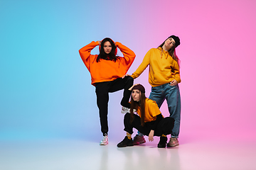 Image showing Girls dancing hip-hop in stylish clothes on gradient background at dance hall in neon light.