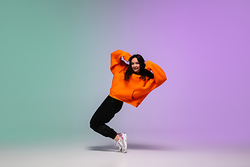 Image showing Girl dancing hip-hop in stylish clothes on gradient background at dance hall in neon light.