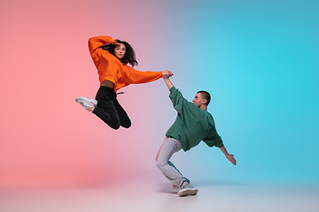 Image showing Boy and girl dancing hip-hop in stylish clothes on gradient background at dance hall in neon light.