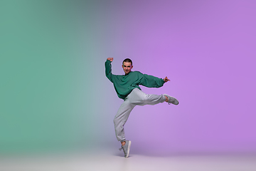 Image showing Boy dancing hip-hop in stylish clothes on gradient background at dance hall in neon light.