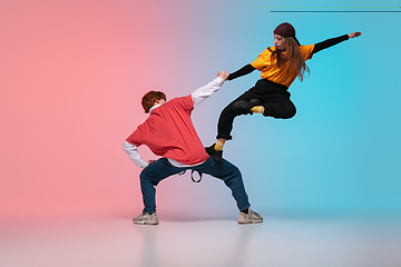 Image showing Boy and girl dancing hip-hop in stylish clothes on gradient background at dance hall in neon light.