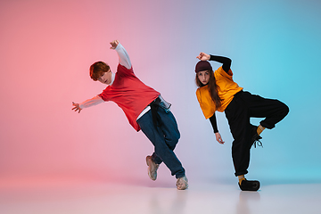 Image showing Boy and girl dancing hip-hop in stylish clothes on gradient background at dance hall in neon light.