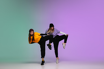 Image showing Girls dancing hip-hop in stylish clothes on gradient background at dance hall in neon light.