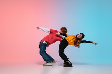 Image showing Boy and girl dancing hip-hop in stylish clothes on gradient background at dance hall in neon light.