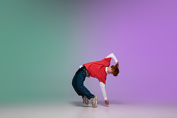 Image showing Boy dancing hip-hop in stylish clothes on gradient background at dance hall in neon light.