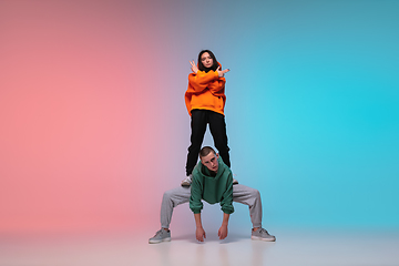 Image showing Boy and girl dancing hip-hop in stylish clothes on gradient background at dance hall in neon light.