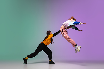 Image showing Girls dancing hip-hop in stylish clothes on gradient background at dance hall in neon light.