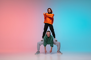 Image showing Boy and girl dancing hip-hop in stylish clothes on gradient background at dance hall in neon light.