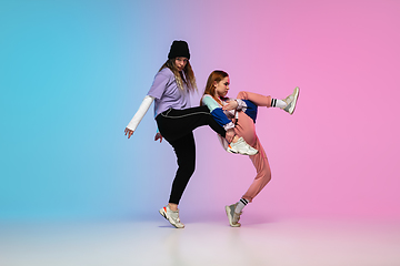 Image showing Girls dancing hip-hop in stylish clothes on gradient background at dance hall in neon light.