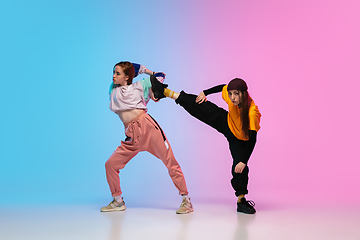 Image showing Girls dancing hip-hop in stylish clothes on gradient background at dance hall in neon light.