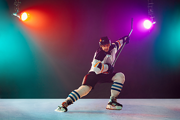 Image showing Male hockey player with the stick on ice court and dark neon colored background