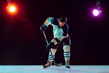 Image showing Male hockey player with the stick on ice court and dark neon colored background