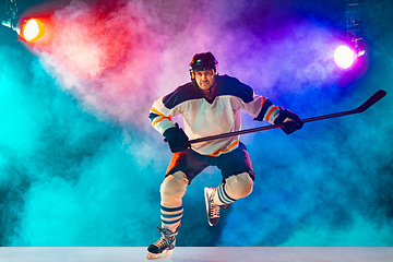 Image showing Male hockey player with the stick on ice court and dark neon colored background