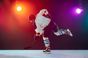 Image showing Male hockey player with the stick on ice court and dark neon colored background