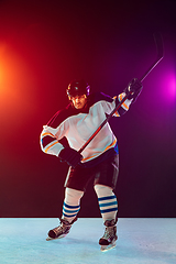 Image showing Male hockey player with the stick on ice court and dark neon colored background