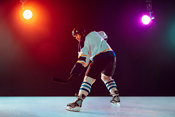 Image showing Male hockey player with the stick on ice court and dark neon colored background