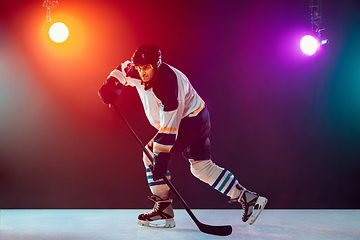 Image showing Male hockey player with the stick on ice court and dark neon colored background