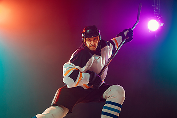 Image showing Male hockey player with the stick on ice court and dark neon colored background