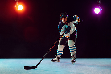 Image showing Male hockey player with the stick on ice court and dark neon colored background