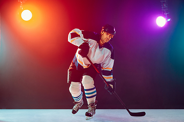 Image showing Male hockey player with the stick on ice court and dark neon colored background