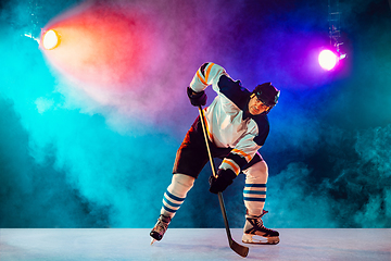 Image showing Male hockey player with the stick on ice court and dark neon colored background