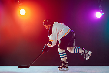 Image showing Male hockey player with the stick on ice court and dark neon colored background