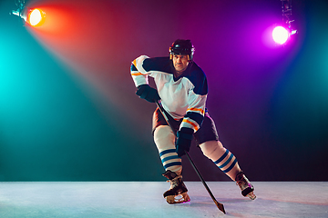 Image showing Male hockey player with the stick on ice court and dark neon colored background