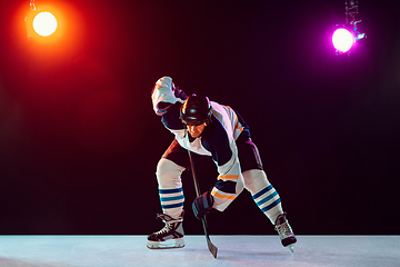 Image showing Male hockey player with the stick on ice court and dark neon colored background