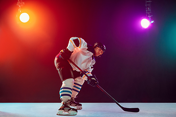 Image showing Male hockey player with the stick on ice court and dark neon colored background