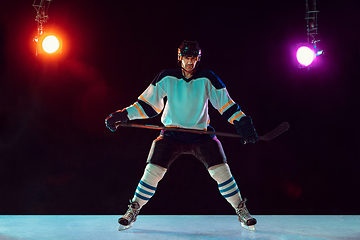 Image showing Male hockey player with the stick on ice court and dark neon colored background