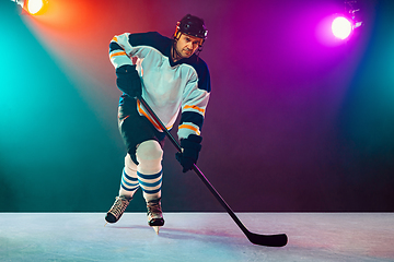 Image showing Male hockey player with the stick on ice court and dark neon colored background