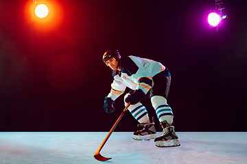 Image showing Male hockey player with the stick on ice court and dark neon colored background