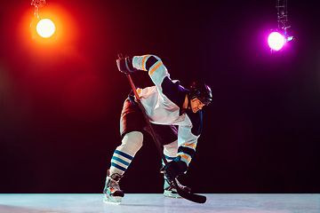 Image showing Male hockey player with the stick on ice court and dark neon colored background