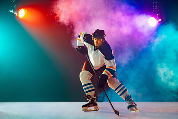 Image showing Male hockey player with the stick on ice court and dark neon colored background