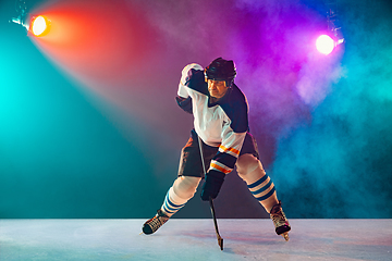 Image showing Male hockey player with the stick on ice court and dark neon colored background