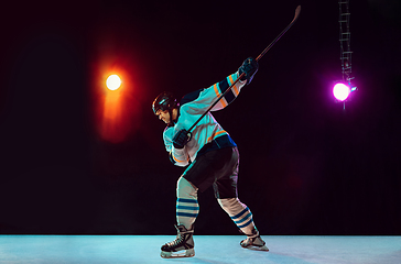 Image showing Male hockey player with the stick on ice court and dark neon colored background