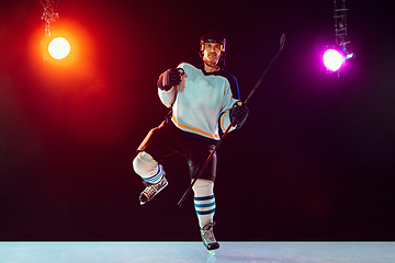 Image showing Male hockey player with the stick on ice court and dark neon colored background