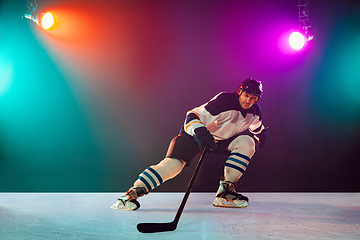 Image showing Male hockey player with the stick on ice court and dark neon colored background