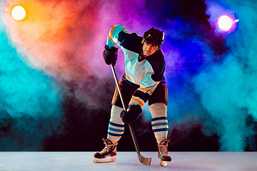 Image showing Male hockey player with the stick on ice court and dark neon colored background