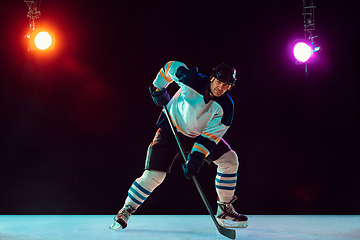 Image showing Male hockey player with the stick on ice court and dark neon colored background