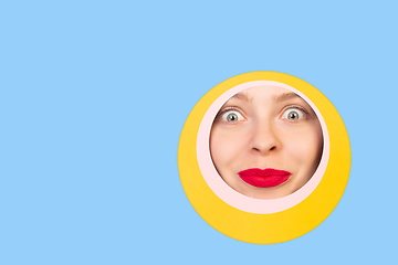 Image showing Female face with red lips peeking throught circle in blue background