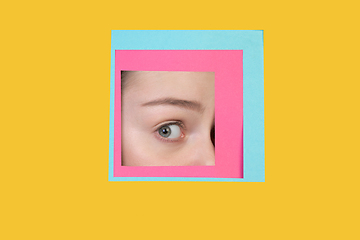 Image showing Face of caucasian woman peeking throught square in yellow background