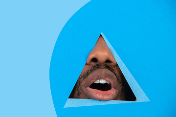 Image showing Lips of african-american man peeking throught triangle in blue background