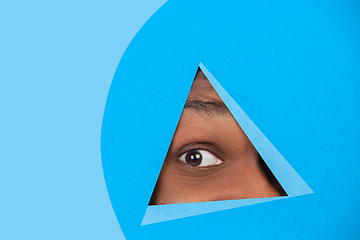 Image showing Eye of african-american man peeking throught triangle in blue background