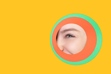 Image showing Female eye peeking throught circle in yellow background