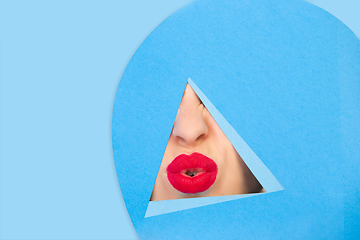 Image showing Female red lips peeking throught triangle in blue background