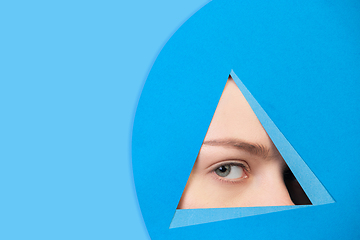 Image showing Face of caucasian woman peeking throught triangle in blue background