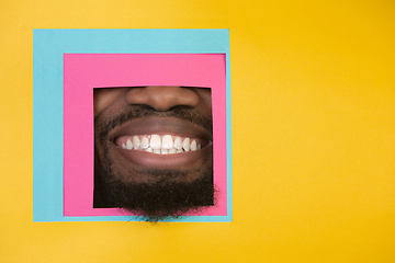 Image showing Mouth of african-american man peeking throught square in yellow background